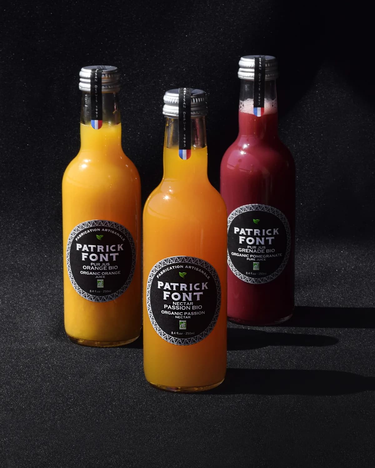Trois bouteilles de jus Patrick Font sur fond sombre